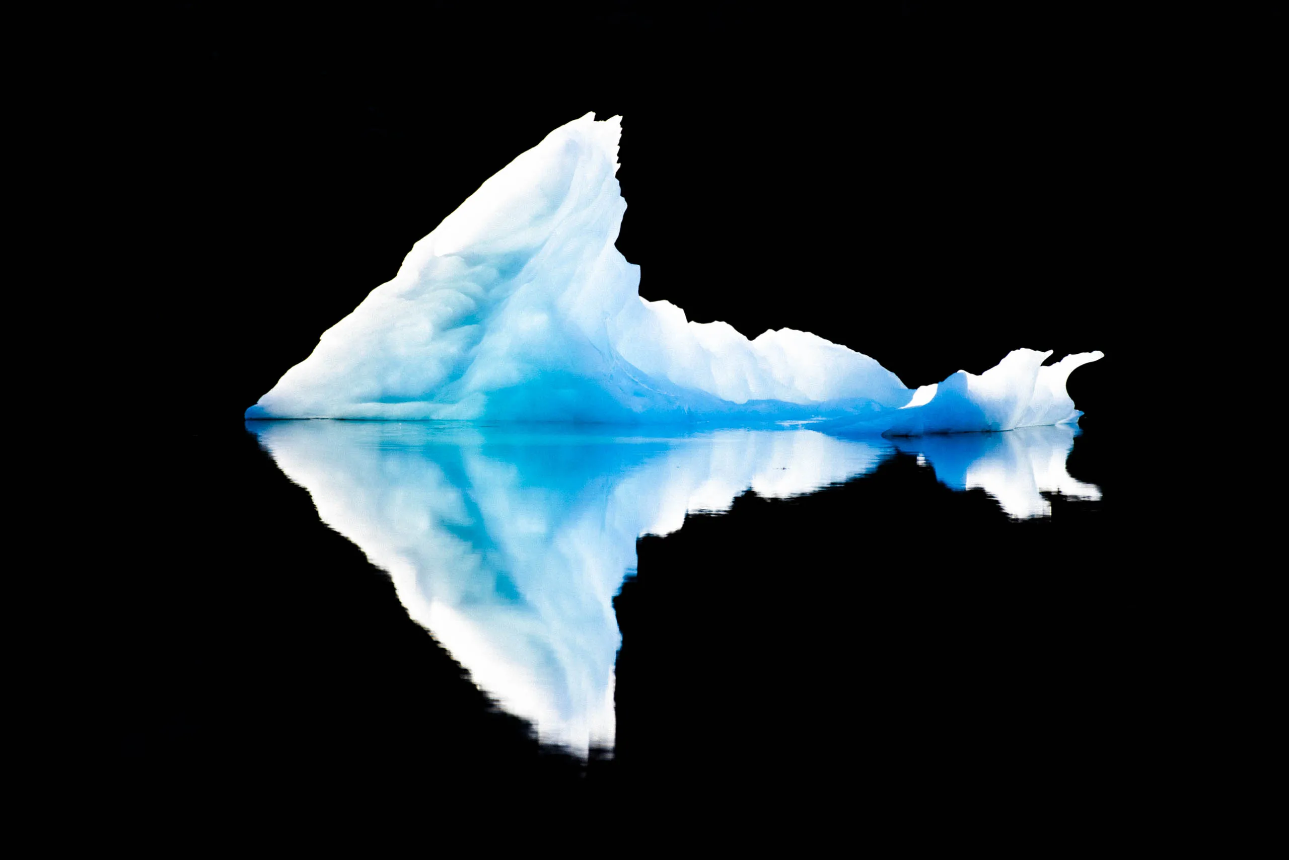 A fine-art photograph of an iceberg and its reflection against the black background of the sea in Greenland.